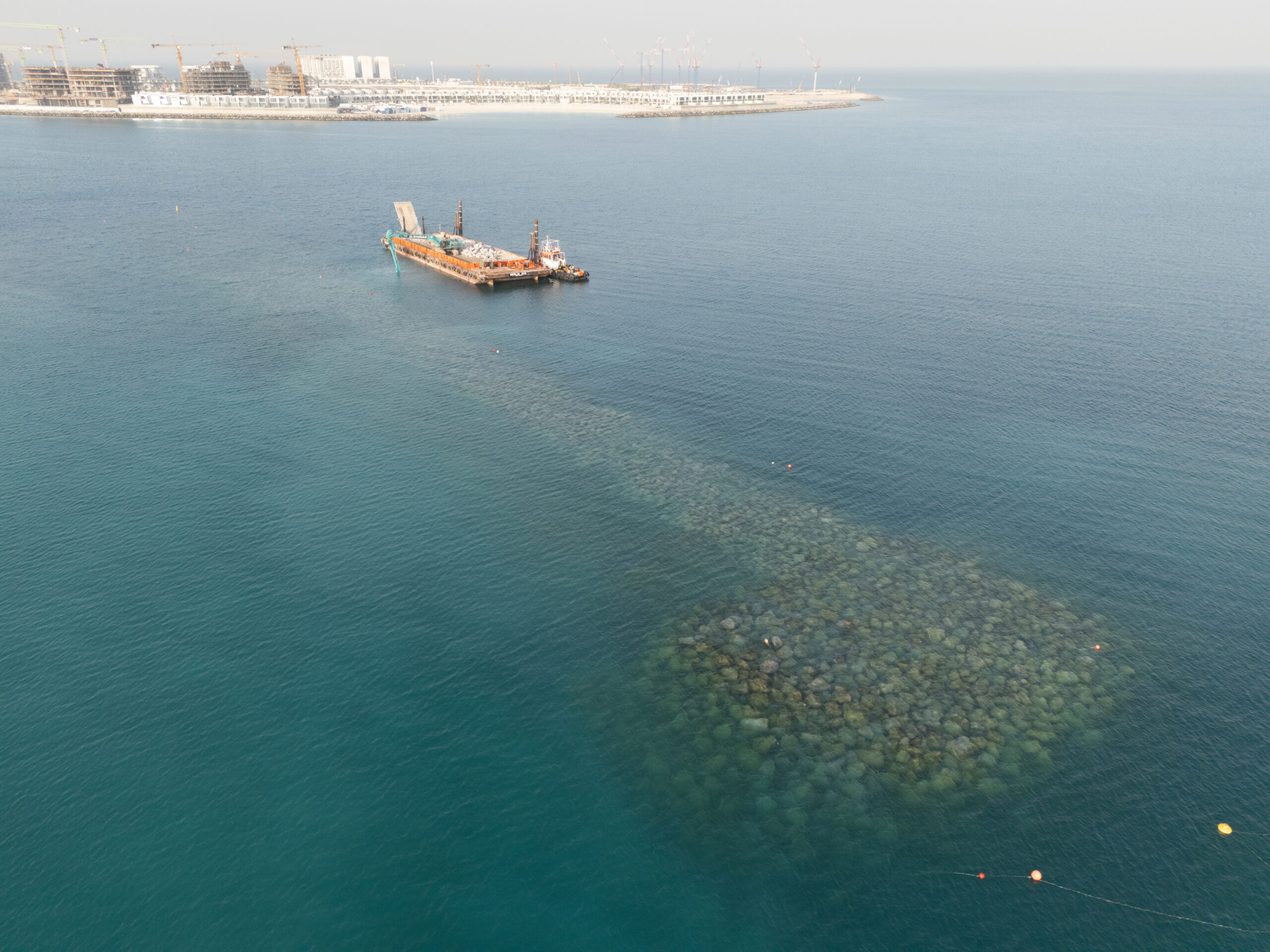 Aerial view of submerged breakwater construction and marine operations in Dubai